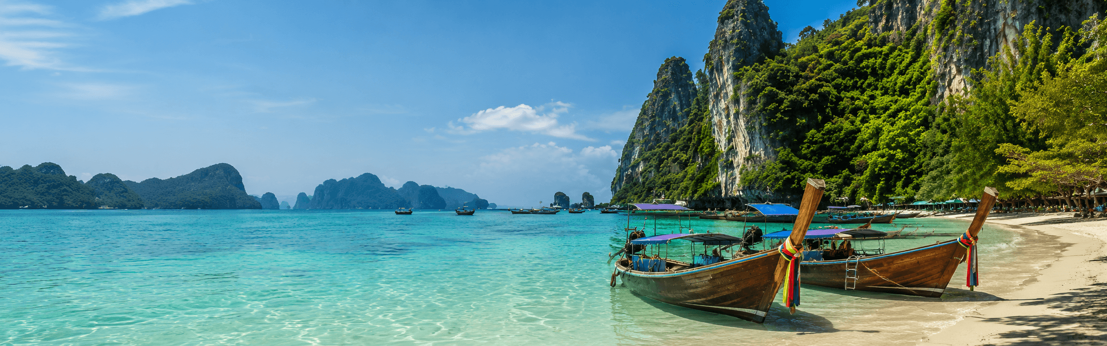Wooden longtail boats on a tropical beach in Thailand with turquoise water and dramatic limestone cliffs in the background.